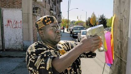 The Rev. Sheldon Stoudemire staples signs on poles along Homewood Avenue in Pittsburgh.