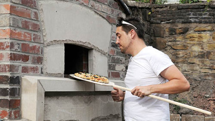 Josh Tonies checks the doness of a pizza.