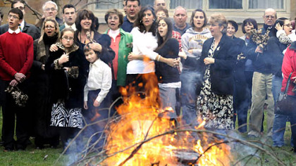 Parishioners from St. Elijah Serbian Orthodox Church in Aliquippa sing carols yesterday as they watch a fire burning a small oak tree for Badnji Day, the day before Orthodox Christmas.