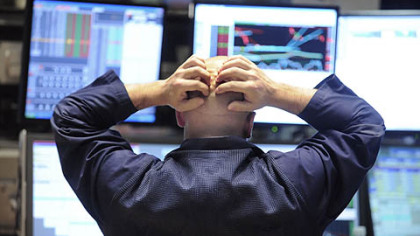 Specialist Justin Bohan holds his head as he works at his post on the floor of the New York Stock Exchange yesterday. Stocks plunged in the final minutes of trading, sending the Dow Jones industrial average down more than 675 points.