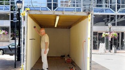 Robert Raczka works on hanging his photographic installation in his container at Market Square earlier this month. He was part of the Three Rivers Arts Festival's "Contained" project.