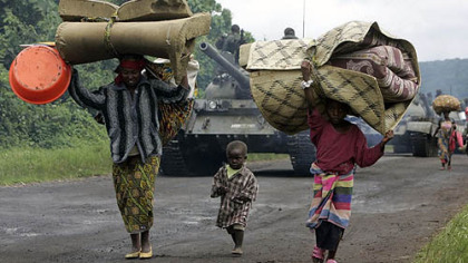 KIMBUMA, Congo -- People walk past a convoy of Congolese army tanks as they flee fighting in eastern Congo. Thousands of refugees and soldiers are fleeing fighting in what appears to be a major retreat of government forces being attacked by rebels of renegade Gen. Laurent Nkunda.