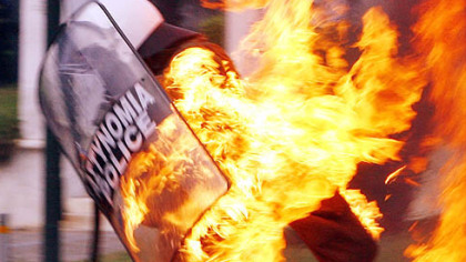 ATHENS, Greece -- A riot policeman is covered in flames from a hand thrown bottle bomb thrown by a rioter, Friday, Dec. 12. His colleagues put out the flames with extinguishers.